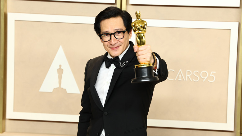 Ke Huy Quan in tux holding Oscar in front of him in front of peach background in 2023