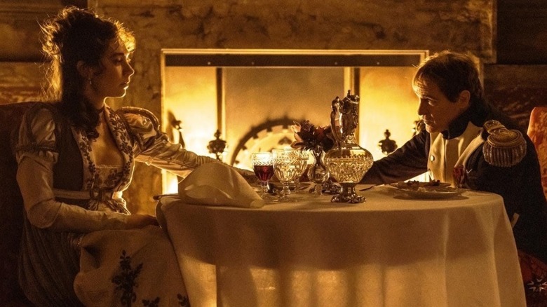 Vanessa Kirby as Josephine sitting across from Joaquin Phoenix as Napoleon at a dinner table in Napoleon