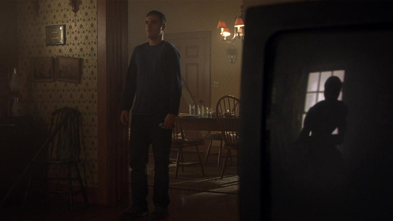 Merrill (Joaquin Phoenix) stands in the doorway; in the reflection of the television, we see an alien in Signs