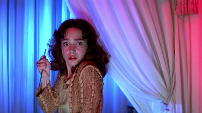 Suzy (Jessica Harper) stands in front of curtains lit blue, purple, and red, in Suspiria