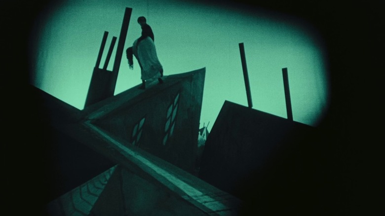 A green-tinted frame from The Cabinet of Dr. Caligari, showing Cesare (Conrad Veidt) carrying an unconscious woman over a rooftop