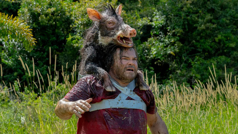 Jack Black as Doug McCallister, walking through a field with a pig strapped to his back in Anaconda 2025