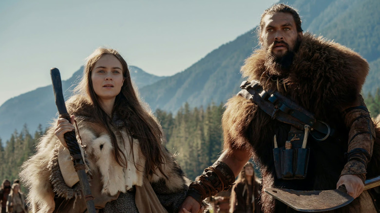 Hera Hilmar and Jason Momoa as Maghra Kane and Baba Voss holding hands outside in See