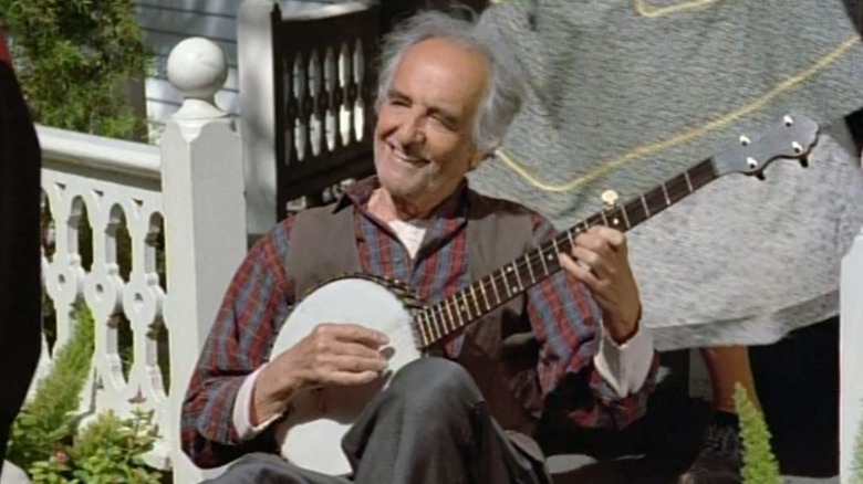 The Caretaker (Basil Langton) smiles while playing the banjo on a porch in Star Trek: Voyager