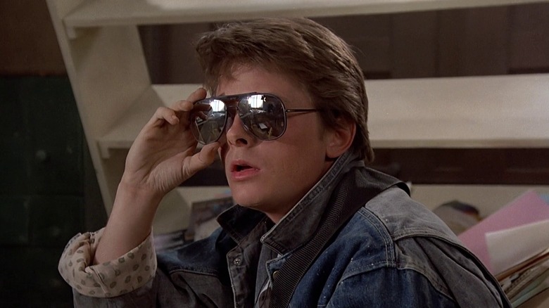 Michael J. Fox as Marty McFly in Back to the Future, looking on in slight shock at something out of frame as he removes his sunglasses.