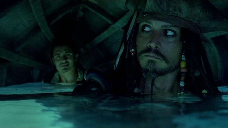 Johnny Depp as Captain Jack Sparrow and Orlando Bloom as Will Turner in Pirates of the Caribbean: The Curse of the Black Pearl, walking through the water under a canoe.
