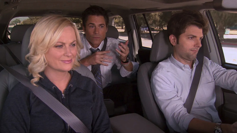 Leslie Knope (Amy Poehler) and Ben Wyatt (Adam Scott) driving with Chris Traeger (Rob Lowe) in the back seat in Parks and Recreation