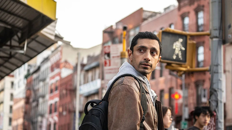 Riz Ahmed as Ash standing on a street corner in Relay