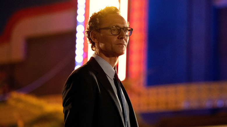 Tom Hiddleston as Charles Krantz standing in the street by neon signs in The Life of Chuck