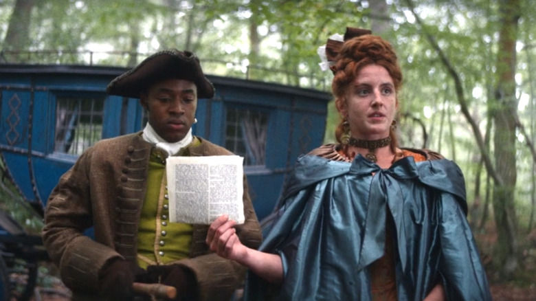 Enyi Okoronkwo as Rasselas stands outside next to Louisa Harland as Nell Jackson who is holding a piece of paper on Renegade Nell