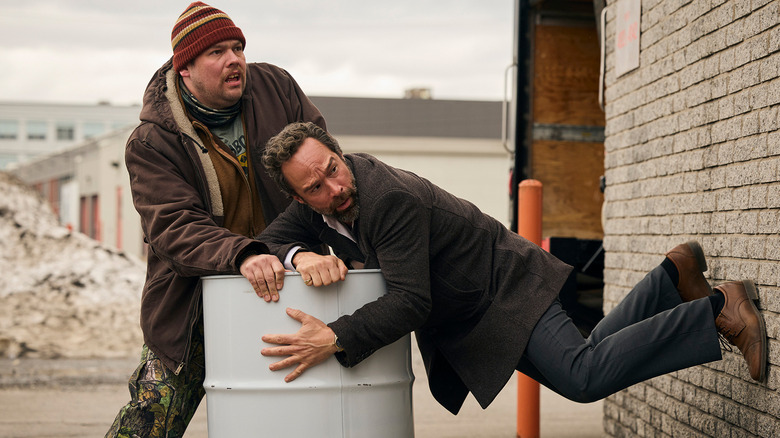 Remy Bouchard (Guillaume Cyr) and Mike Byrne (Chris Diamantopoulos) awkwardly hold a barrel of syrup in The Sticky