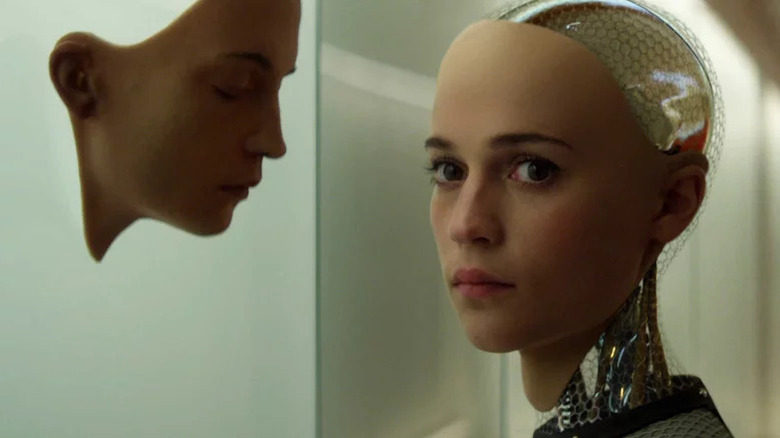 Alicia Vikander as Ava with mechanical head and neck exposed standing next to mask of her face in Ex Machina