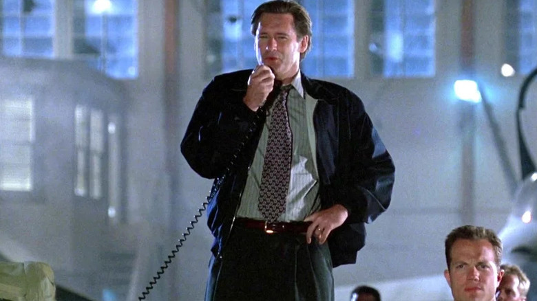 Bill Pullman as President Whitmore talking into corded microphone with Adam Baldwin as Major Mitchell standing below him in Independence Day