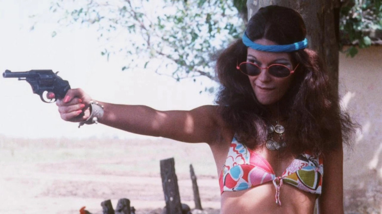 Margarita Amuchástegui as Angelica in sunglasses and headband pointing a gun in Snuff