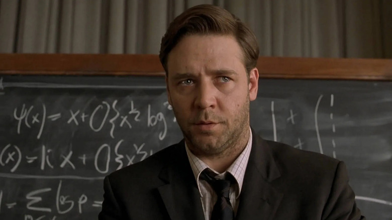 Russell Crowe in suit standing in front of blackboard with math on it in A Beautiful Mind