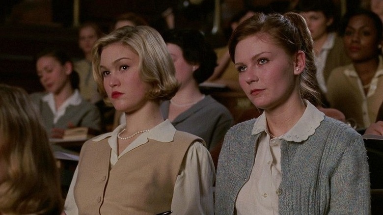 Julia Stiles with short blonde hair as Joan next to Kirsten Dunst as Betty with red hair in ponytail sitting in 1950s lecture hall in Mona Lisa Smile