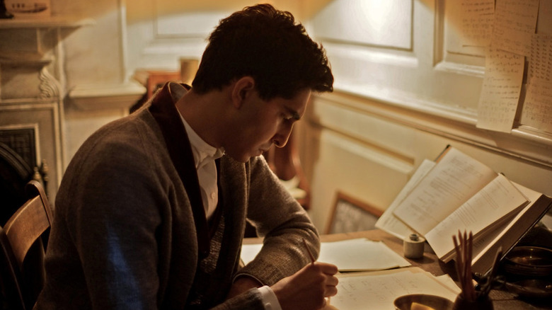 Dev Patel as Srinivasa Ramanujan sitting at desk writing in The Man Who Knew Infinity