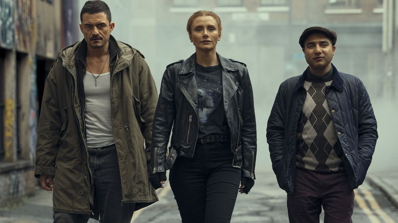 Marlon (Orlando Bloom), Kat (Bryce Dallas Howard), and Hugh (Nick Mohammed) walking in a smoggy alley in Deep Cover