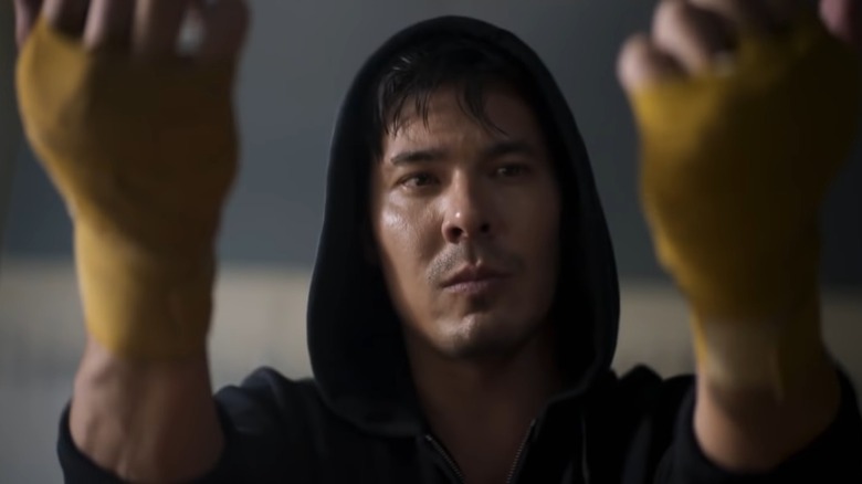 Lewis Tan as Cole Young looking down at yellow gloves on his hands in Mortal Kombat