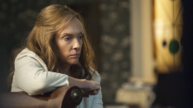 Annie Graham (Toni Collette) sits pensively leaning on a chair in Hereditary