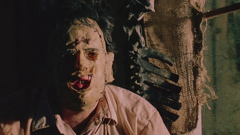 Leatherface (Gunnar Hansen) stands staring by a skeleton in The Texas Chain Saw Massacre