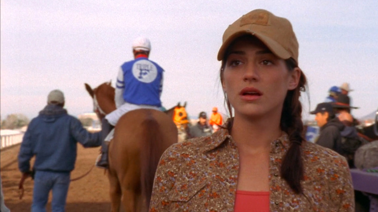 Genevieve Cortese as Kris wearing baseball cap with horse and jockey behind her in Wildfire