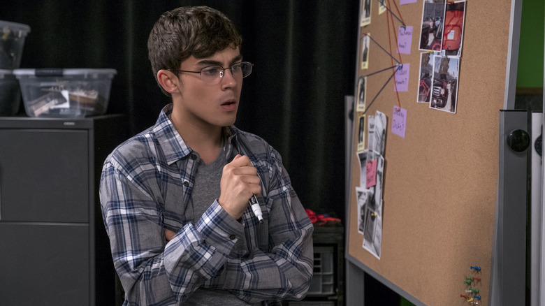 A teenager stands in front of a murder board