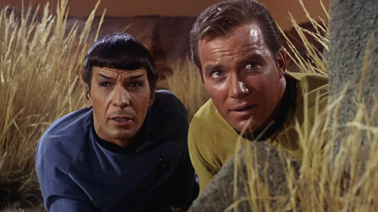 Spock (Leonard Nimoy) and James Kirk (William Shatner) crouch behind a rock in Star Trek: The Original Series