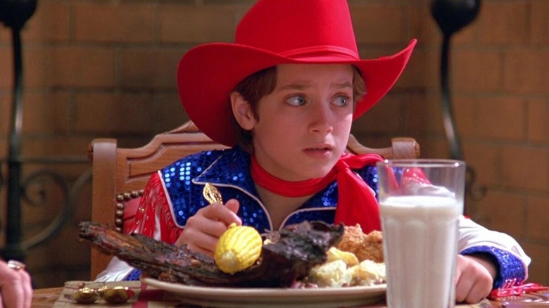 Elijah Wood as North sits at a table dressed like a cowboy in North