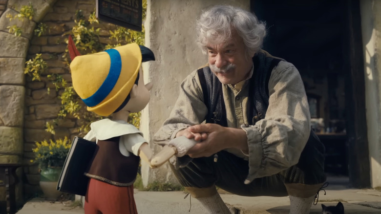 Tom Hanks as Geppetto shakes Pinocchio's hand in Pinocchio