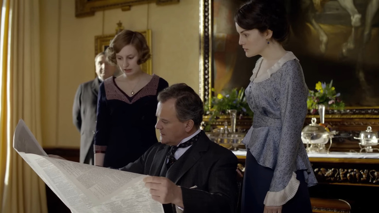Edith (Laura Carmichael) and Mary (Michelle Dockery) look at the newspaper over their father's shoulder in Downton Abbey