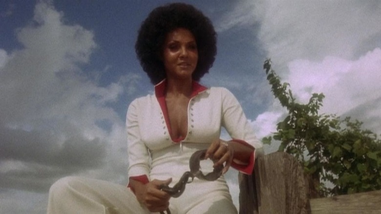 Sugar Hills holds handcuffs and sits on a fence looking triumphant