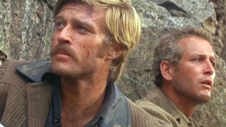 The Sundance Kid (Robert Redford) and Butch Cassidy (Paul Newman) look around from behind a rock in Butch Cassidy and the Sundance Kid