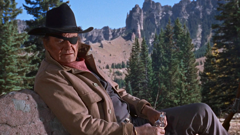 Rooster Cogburn (John Wayne) looks concerned while leaning against a rock in True Grit (1969)