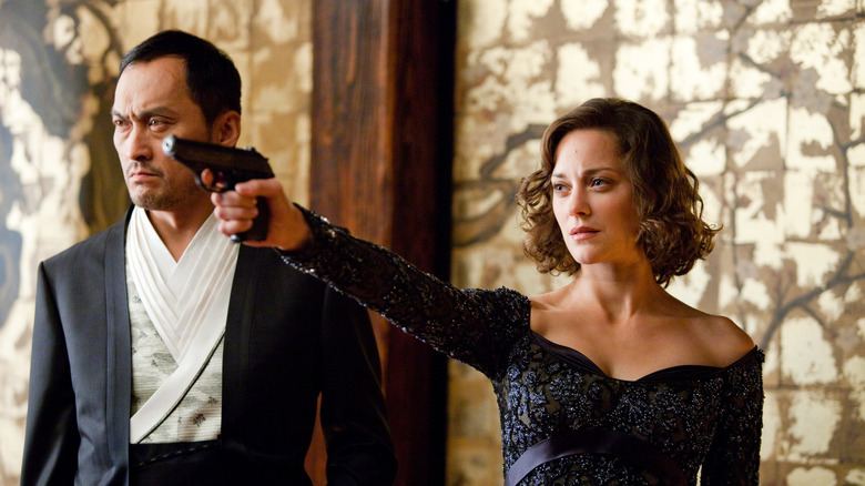 Ken Watanabe's Saito standing next to Marion Cotillard's Mal holding a gun in Inception