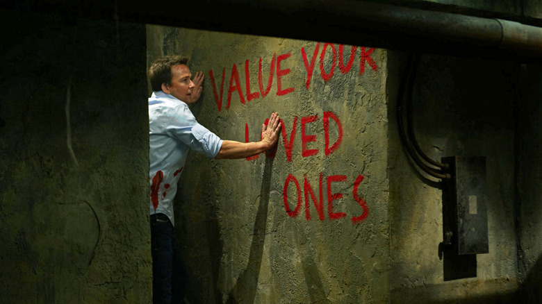 Sean Patrick Flanery as Bobby touching the wall that reads "Value your loved ones" in Saw 3D