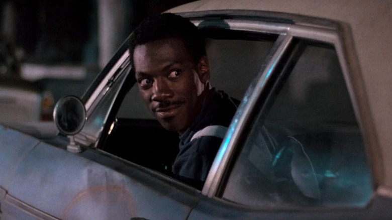 Axel Foley (Eddie Murphy) looks back from his driver's seat smirking in Beverly Hills Cop
