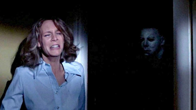 Laurie cries in fear as Michael Myers lurks around the corner