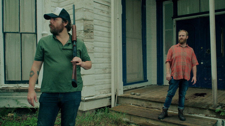 Man with gun standing outside rundown house