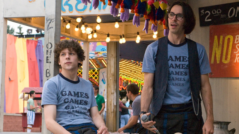 Jesse Eisenberg as James and Martin Starr as Joel in Adventureland, wearing their signature GAMES t-shirt uniforms and looking off at something out of frame.