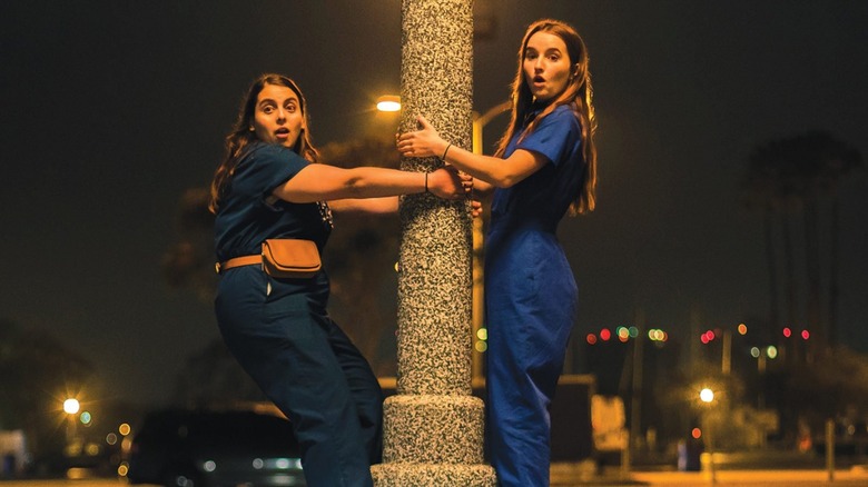 Amy (Kaityn Dever) and (Molly) Beanie Feldstein in Booksmart, holding on to opposite sides of a street lamp and looking shocked off at something out of frame.