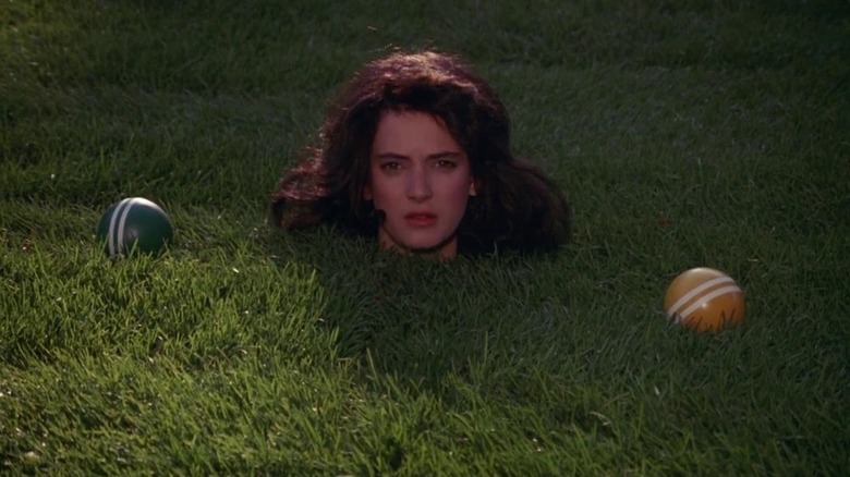 Winona Ryder as Veronica in Heathers, her head sticking out of the grass with some bocce balls around her.
