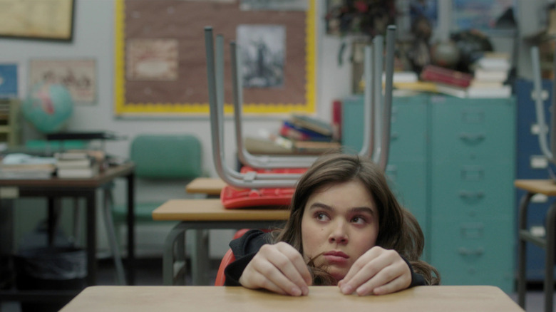 Hailee Steinfeld  as Nadine in a classroom sitting low in a chair in The Edge of Seventeen, sunken down as far as she can go into a desk chair.