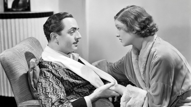 William Powell as Nick Charles in a chair speaking to Myrna Loy as Nora Charles in The Thin Man