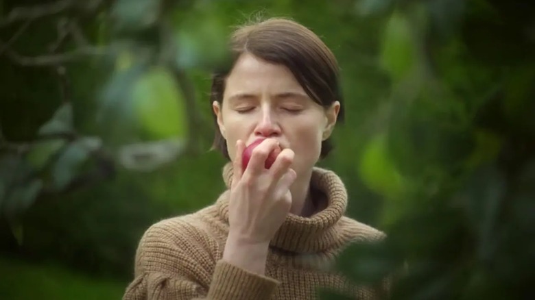 Jessie Buckley, as Harper, eats an apple in a garden, in Men