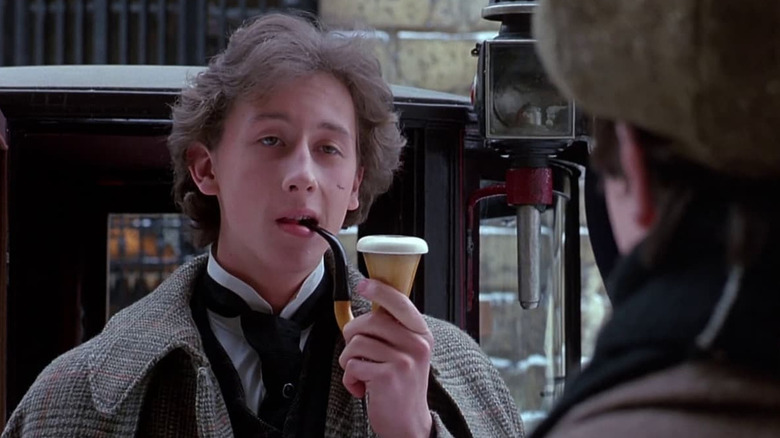 Holmes (Nicholas Rowe) smokes a pipe next to a carriage in Young Sherlock Holmes