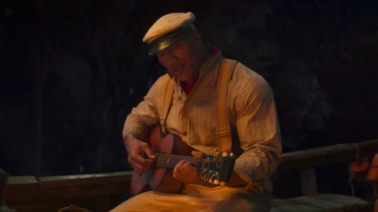 Dwayne Johnson as Frank Wolff, strumming a guitar on a boat in Jungle Cruise