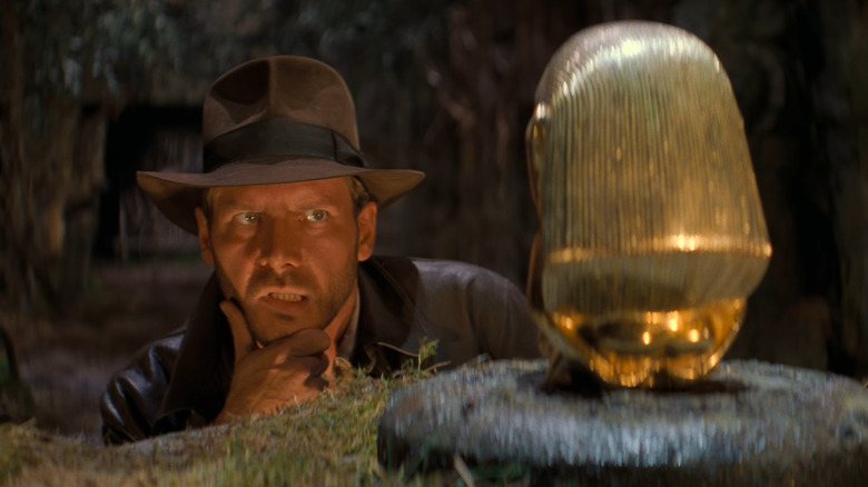 Harrison Ford as Indiana Jones, looking at a golden idol in Raiders of the Lost Ark