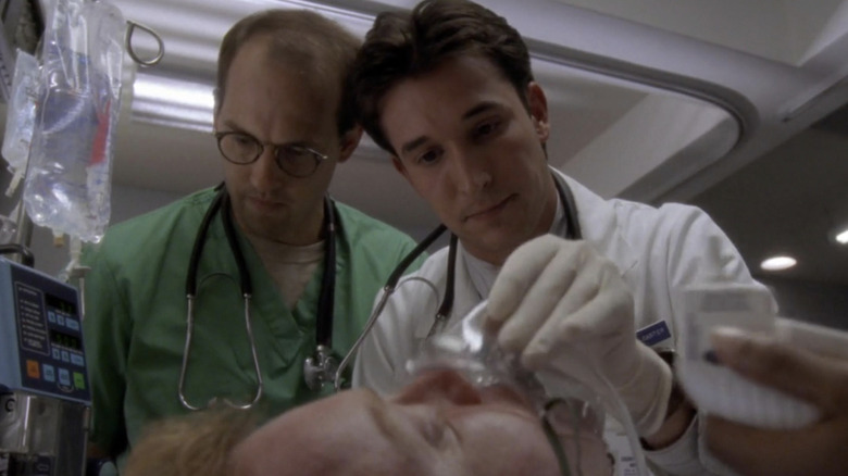 Anthony Edwards as Dr. Mark Greene and Noah Wyle as Dr. John Carter putting an oxygen mask on a patient in ER