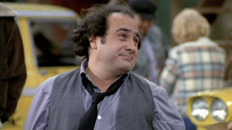 Danny DeVito as dispatcher Louie De Palma standing in front of a taxi cab in Taxi